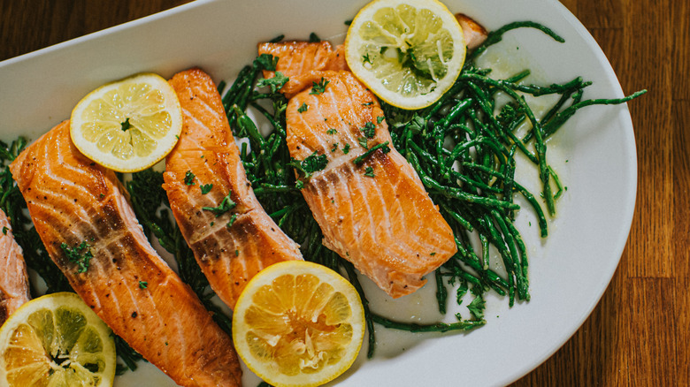 Cooked salmon with lemon slices and greens on a plate