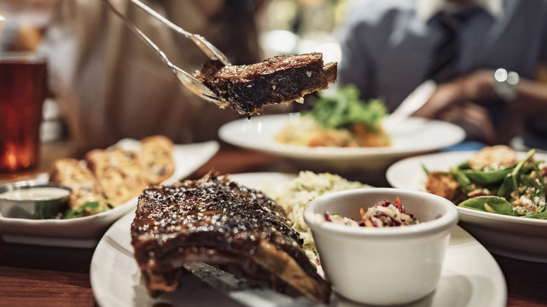 Tongs lifting steak off a plate at a steakhouse with other plates of food in the background