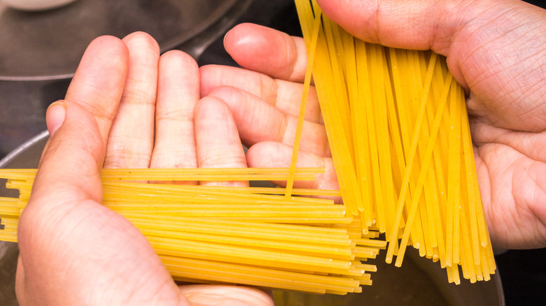 Hands holding strands of broken spaghetti.