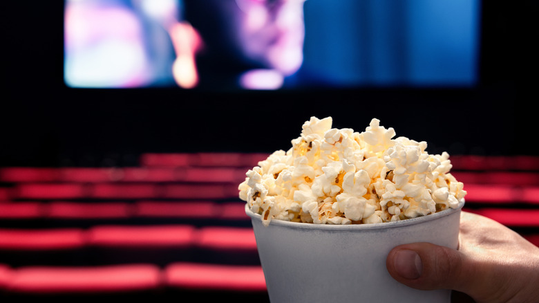 A person holding bucket of popcorn in a movie theater.