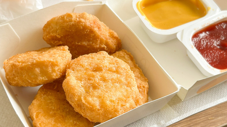 A box of chicken nuggets with dipping sauces next to them.