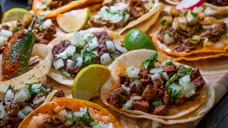 Tacos in corn tortillas with white onion, cilantro and lime garnishes