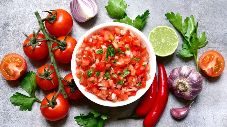 Bowl of salsa surrounded by limes, tomatoes, peppers, and cilantro