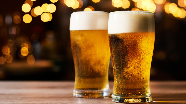 Two glasses of beer with full head of foam.