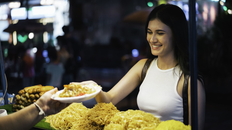 a woman accepting a plate of pad that at a night market