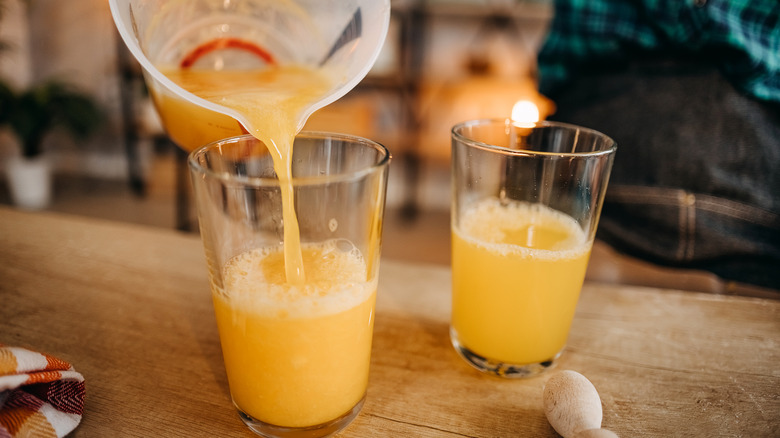 someone pouring orange juice into two glasses from a plastic pitcher