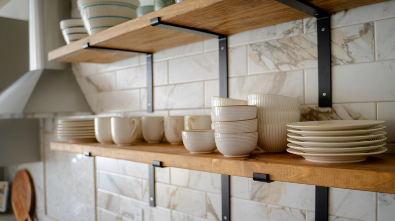 Close up of metal and wood open shelf design with various mugs and flatware on display.