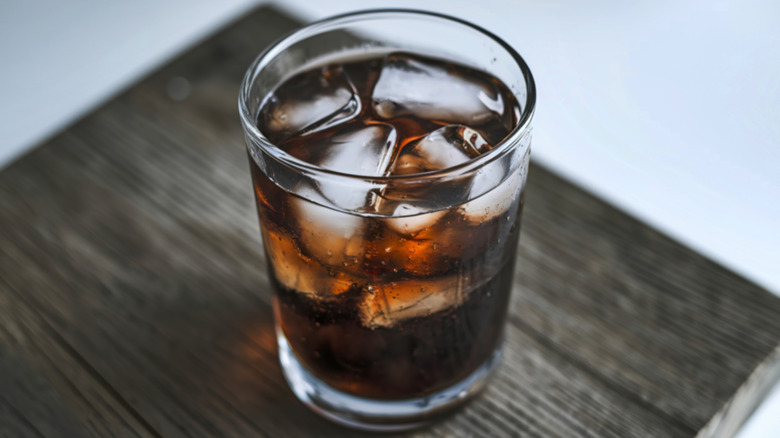 A tall glass filled with cola and ice cubes