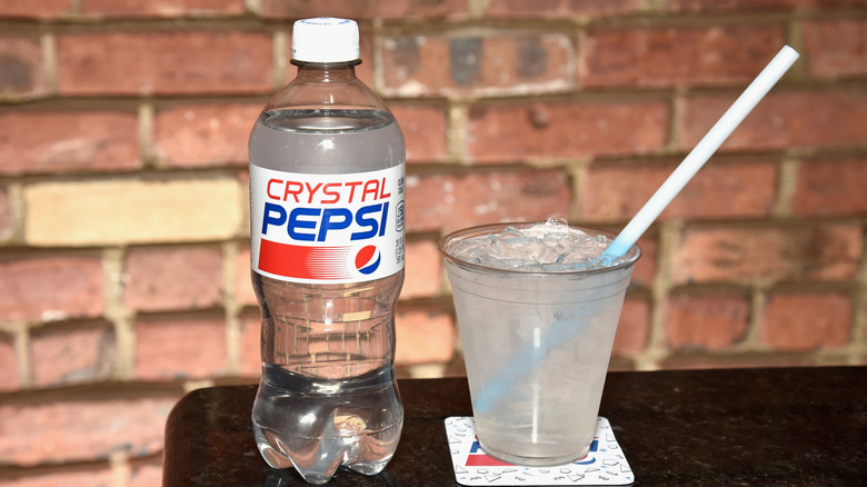 A bottle of crystal pepsi next to a glass of the soda.