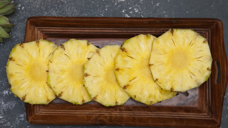 Sliced pineapple rings on wooden cutting board