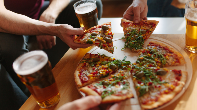 A group of friends drinking beer and eating pizza.