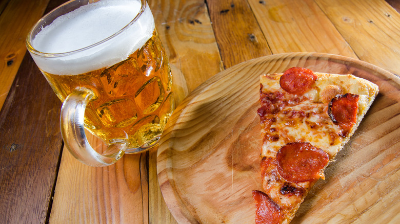Beer and pepperoni pizza on a wooden table.