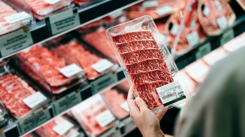 Shopper holding pack of meat in a supermarket deli aisle