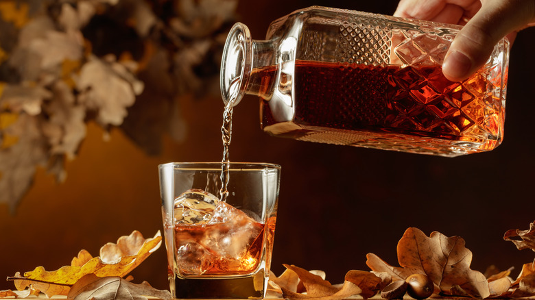 hand pouring whiskey into a glass with ice