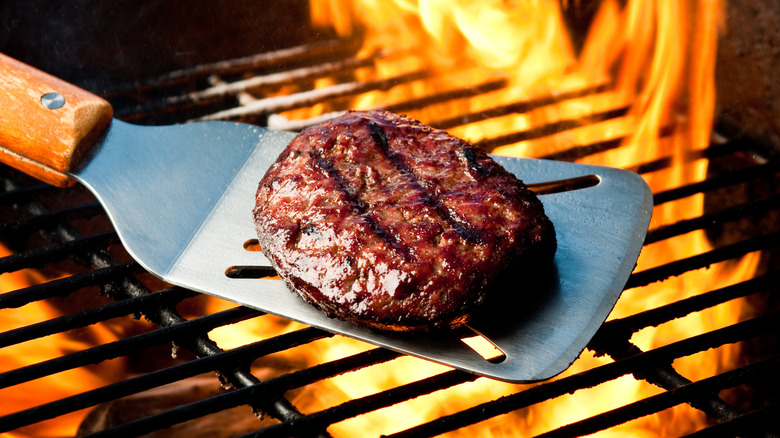 A cooked burger sits on a spatula over an open flame.