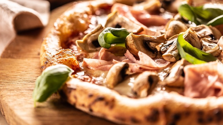 Close-up of artisan pizza with basil, mushrooms, and ham
