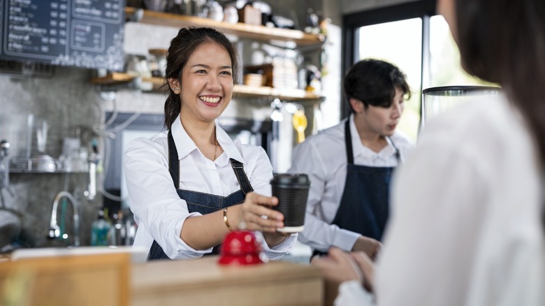 A smiling barista handing a coffee to a customer