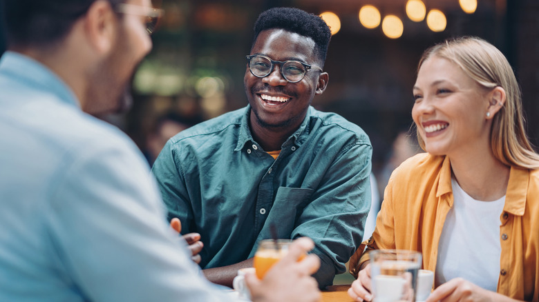 A group of friends laugh with drinks in hand at a restaurant