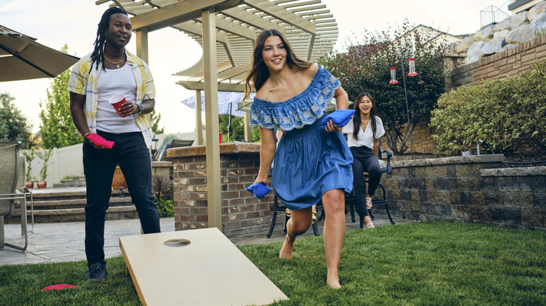 Friends play cornhole on a grass lawn