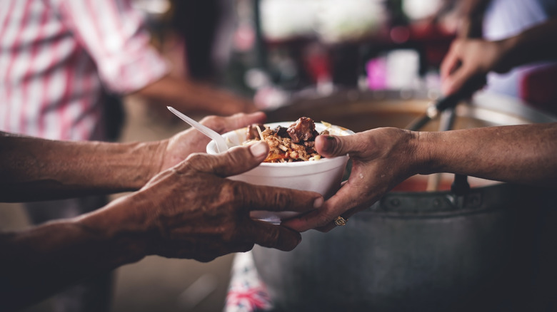 One person handing a bowl of hot food to another person