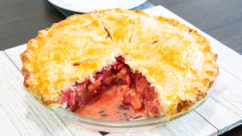 Cross section of freshly baked strawberry and rhubarb pie on wood table.