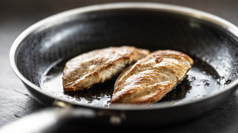 Chicken breast cooked in oil in nonstick pan positioned on counter.