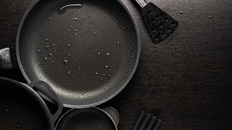 Black nonstick cookware, next to cooking utensils on black countertop.
