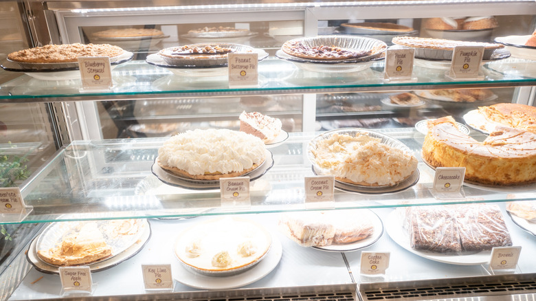 Various pies, including peanut butter cup, pecan, pumpkin, banana cream, and coconut cream, sit inside a glass display case in a diner