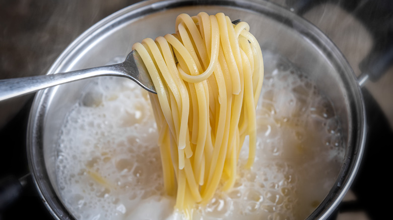 A fork pulling noodles out of a pot of boiling water.