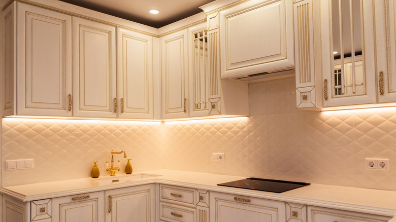 A clean, white kitchen adorned with gold hardware and under-cabinet lighting