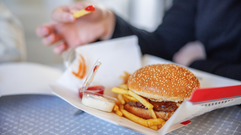 A person eating a take-out burger with fries