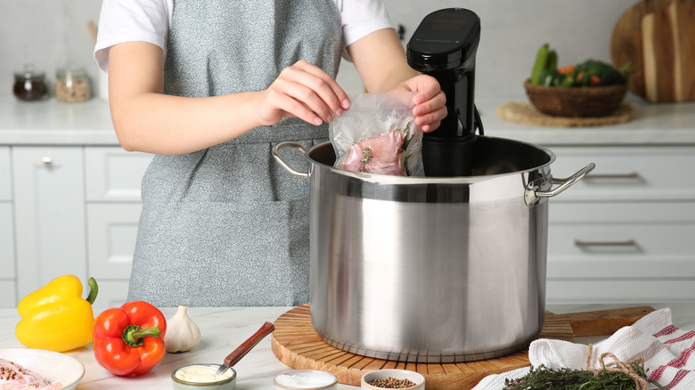 A woman placing a bag of food into a cooking pot with a sous vide immersion circulator attached..