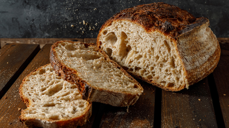 A fresh loaf of wholewheat sourdough bread on a slatted wooden countertop with two pieces sliced off.