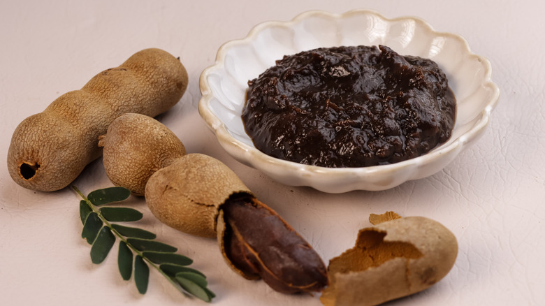 Tamarind paste in white bowl next fresh tamarind pods