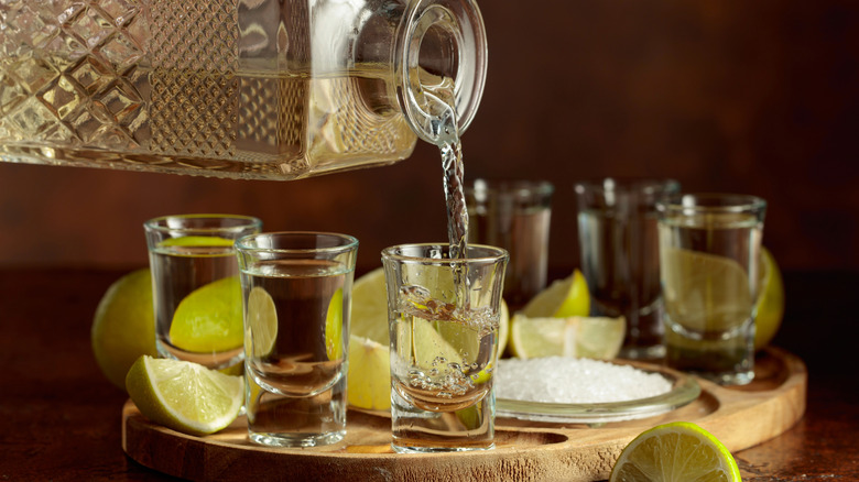 Tequila being poured from a glass decanter into shot glasses.