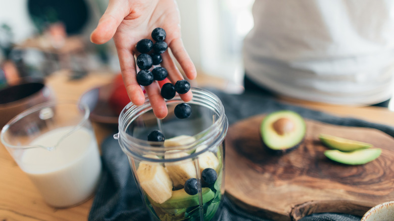 Close-up shot of someone dropping blueberries into a blender