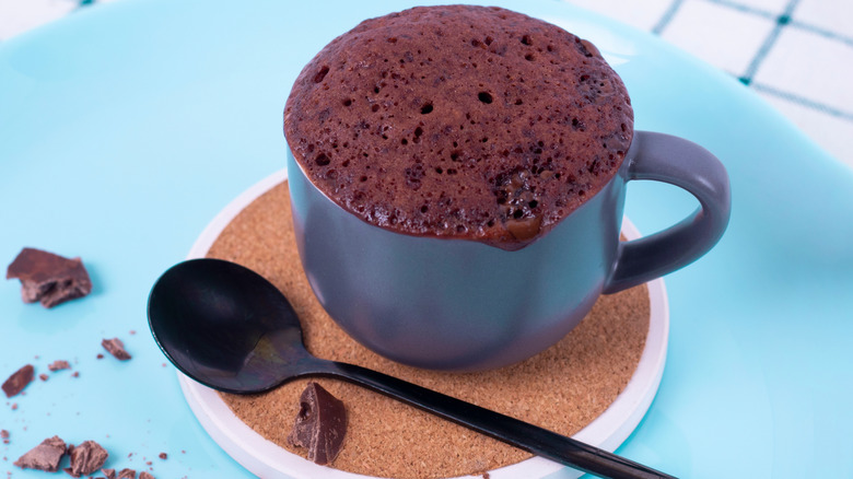 microwaved chocolate mug cake in a blue mug next to a spoon