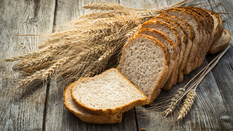 Sliced whole wheat bread with wheat stems beside it on a wood surface