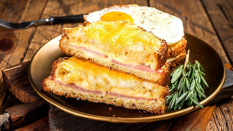 Halved croque madame sandwich on a dark plate with sprigs of fresh rosemary