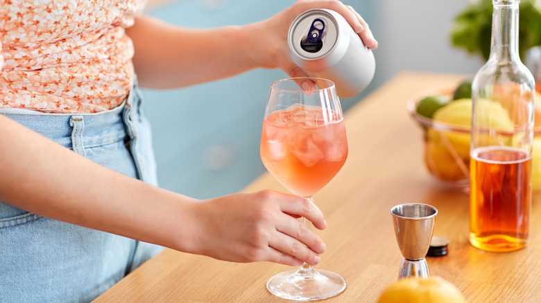 person pouring drink from a can into wine glass