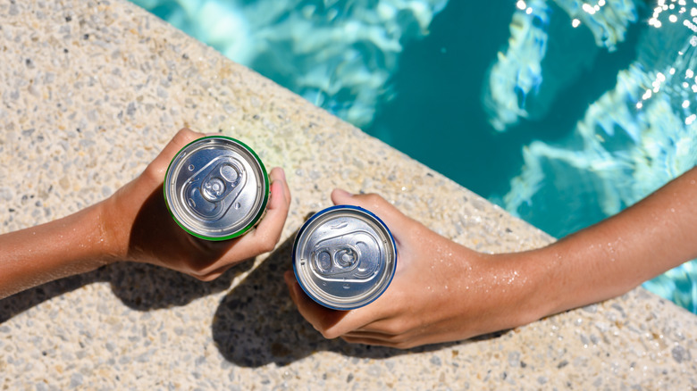 hands holding cans by the pool