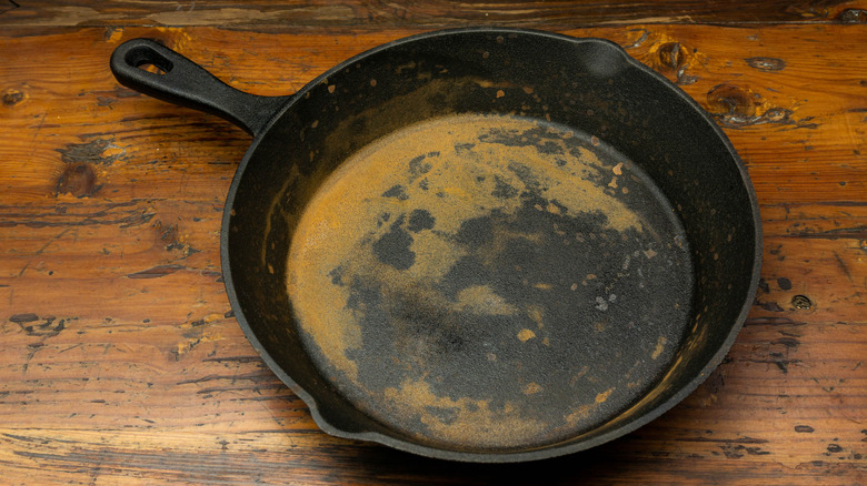 A rusty, used cast iron pan on a wooden tabletop, ready to be cleaned and seasoned.