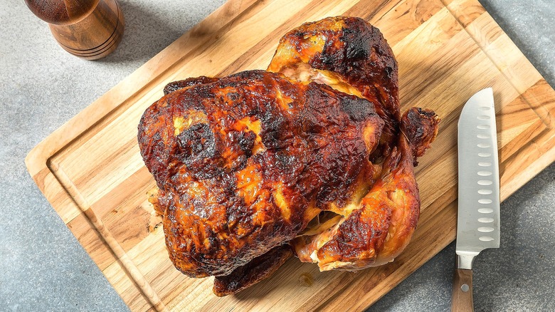 A fully-cooked roasted chicken and carving on a wooden cutting board