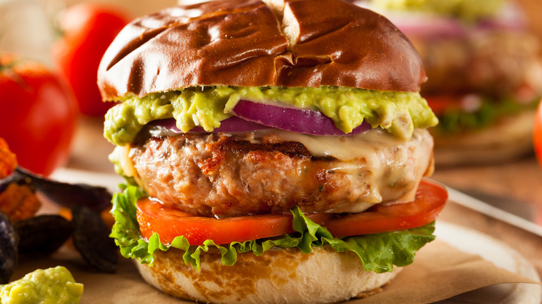 A turkey burger with lettuce, tomato, onion, and guacamole