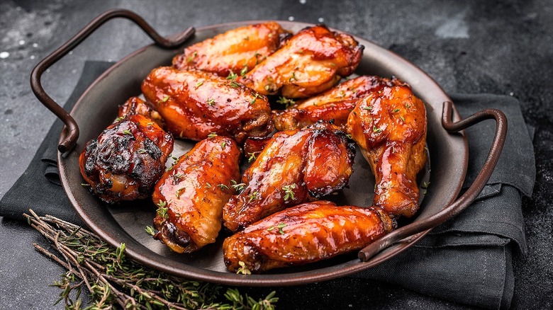 Chicken wings are smothered in barbecue sauce on a dark-coated plate with metal handles
