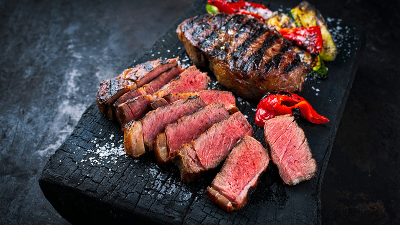 Cooked Wagyu beef with vegetables on a slab of charred wood.