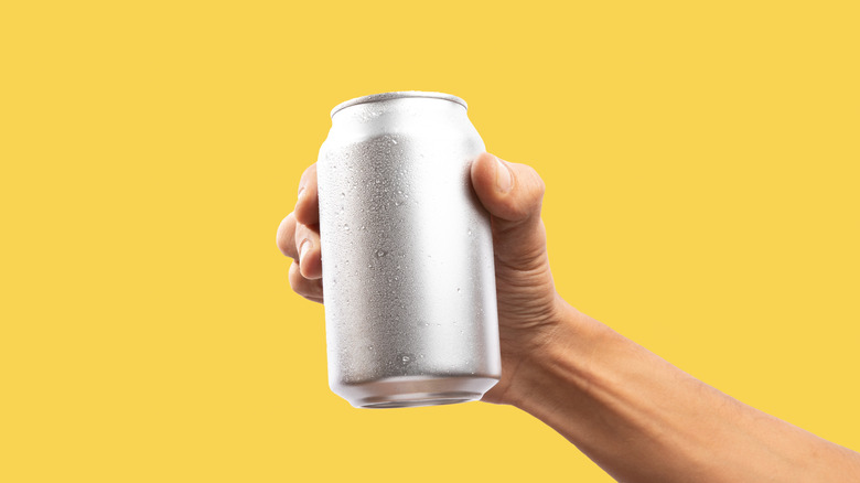 hand holding aluminum can isolated on a yellow background