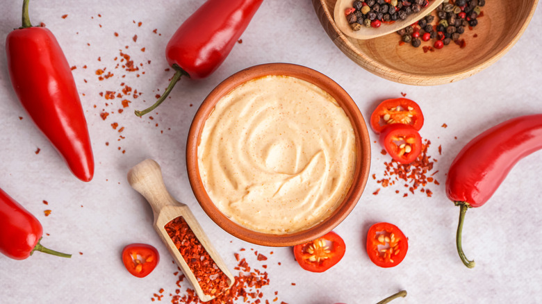 Chipotle sauce in a bowl next to various whole and sliced red peppers