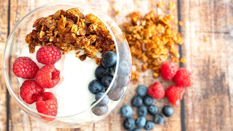 Top-down view of a clear wine glass filled with yogurt, granola, raspberries, and blueberries