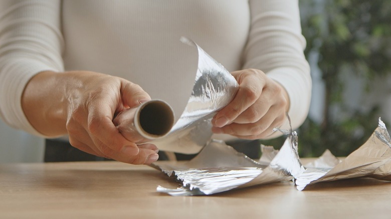 Person pulling strips of aluminum foil off the roll.